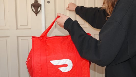 a doordash worker with a red bag knocking on a white front door
