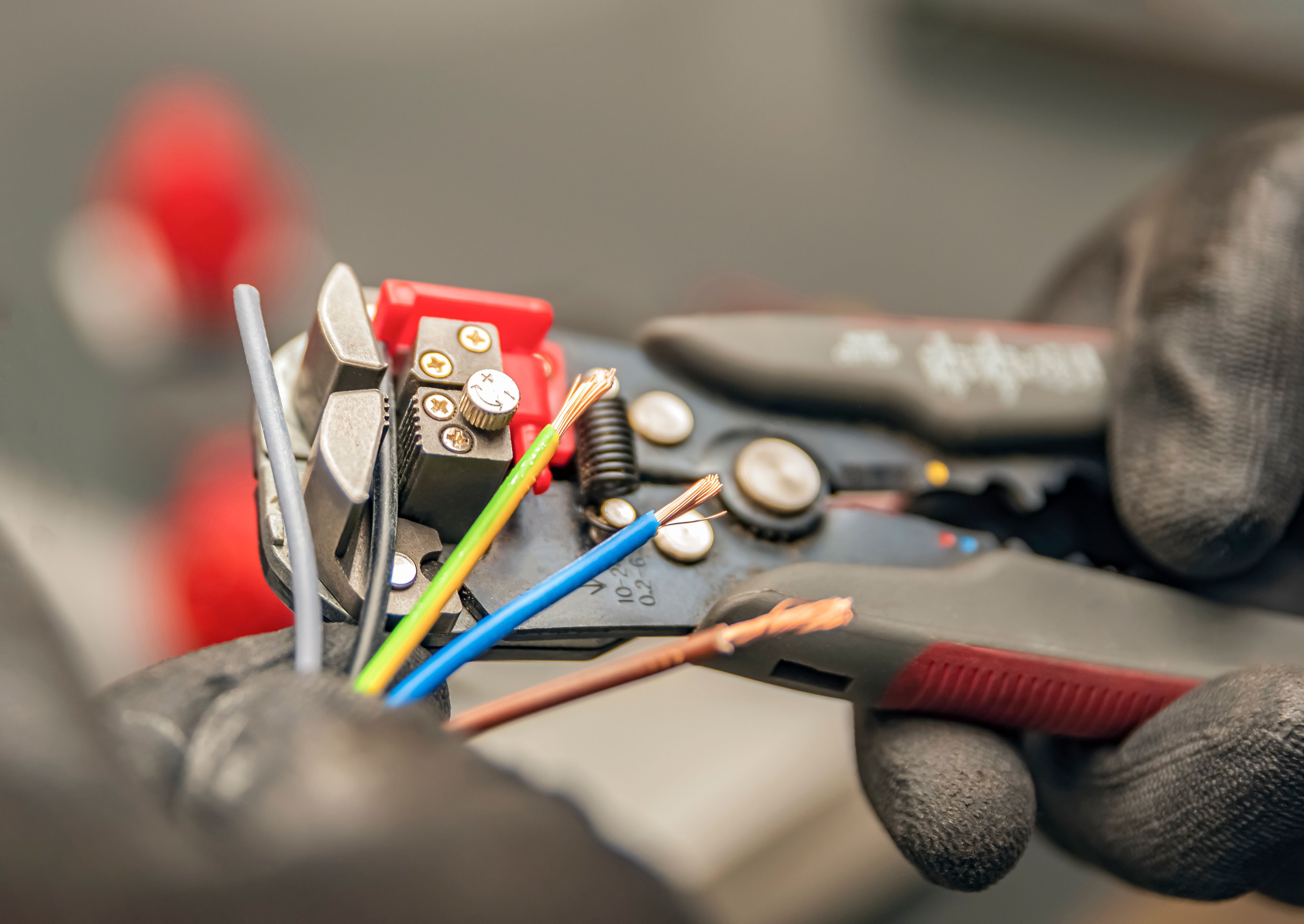 Close-up of electrician’s hands using wire strippers on coloured electrical cables