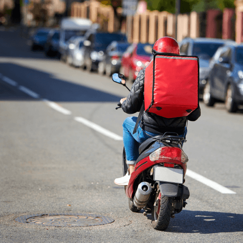 Delivery motorcyclist in red driving up a road