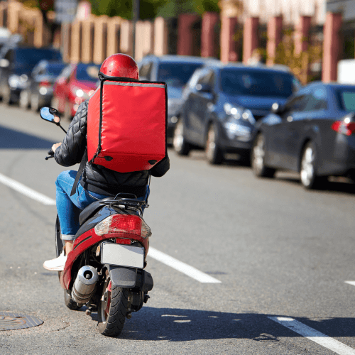 Delivery motorbiker in red driving up road (1)