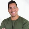 A young man in an olive t shirt, with black hair smiling at the camera against a plain white background.

