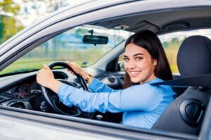 Cute young lady happy driving car. Image of beautiful young woman driving a car and smiling. Portrait of happy female driver steering car with safety belt