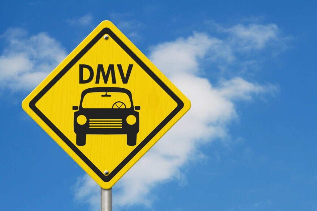 a yellow streetsign with a black car icon on it. the sign reads DMV