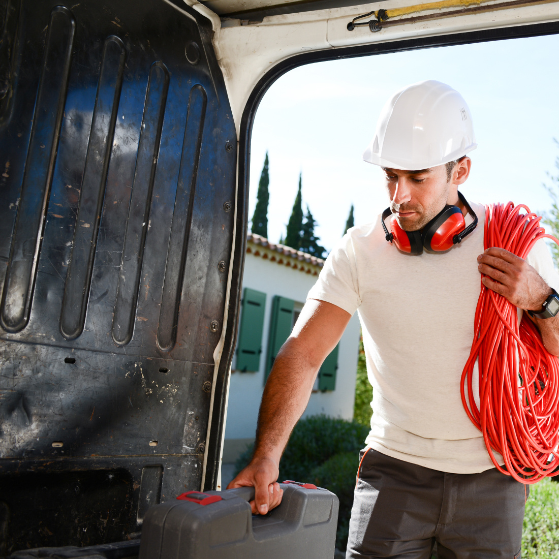 Man in white shirt and helmet retrieving tools from his van