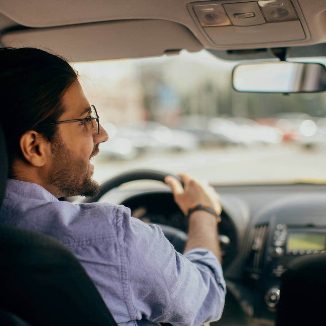 Back view of a man in a pale blue shirt driving a car