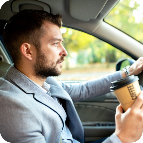 Side view of man in a gray suit driving a car while holding a cardboard coffee cup