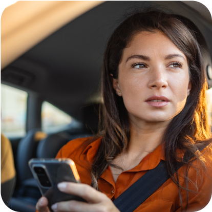 Woman in orange shirt sitting in the driver's seat of her car holding her phone and looking to side