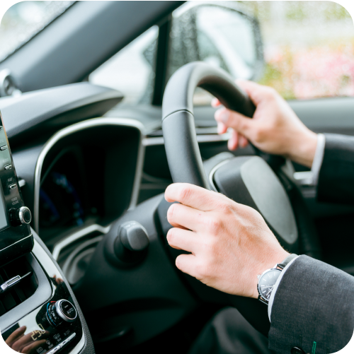 Person wearing suit with his hands on a steering wheel