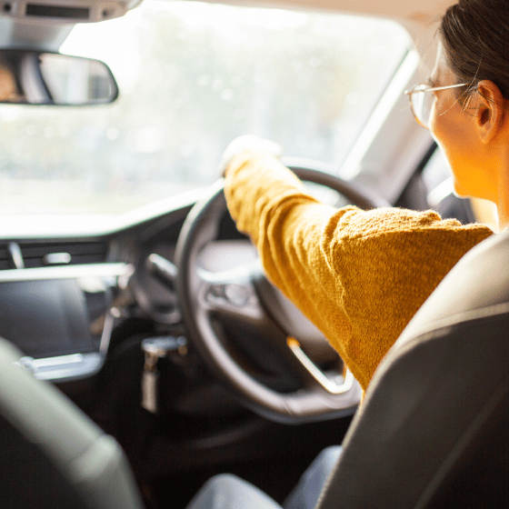 Woman in glasses and yellow jumper driving car