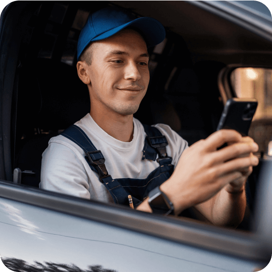 Smiling delivery driver in overalls and a blue cap looking at his phone