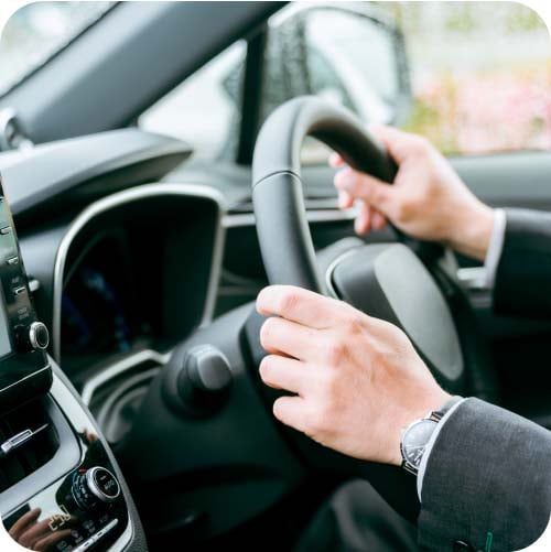 person wearing suit with hands on steering wheel