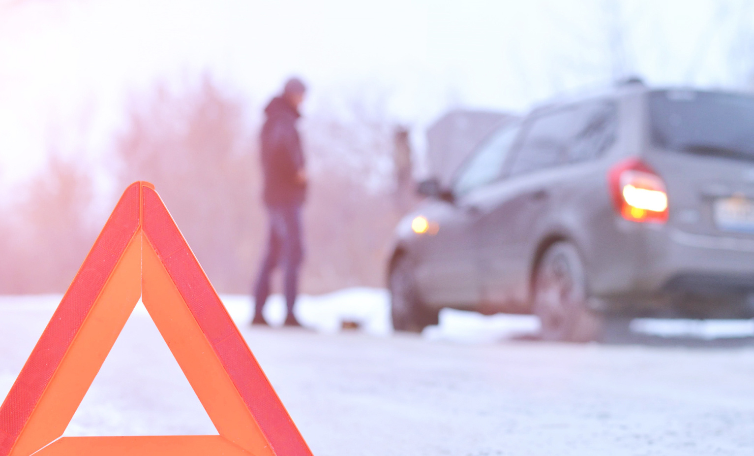 an orange breakdown triangle in the foreground. In the background is a broken down car in the snow