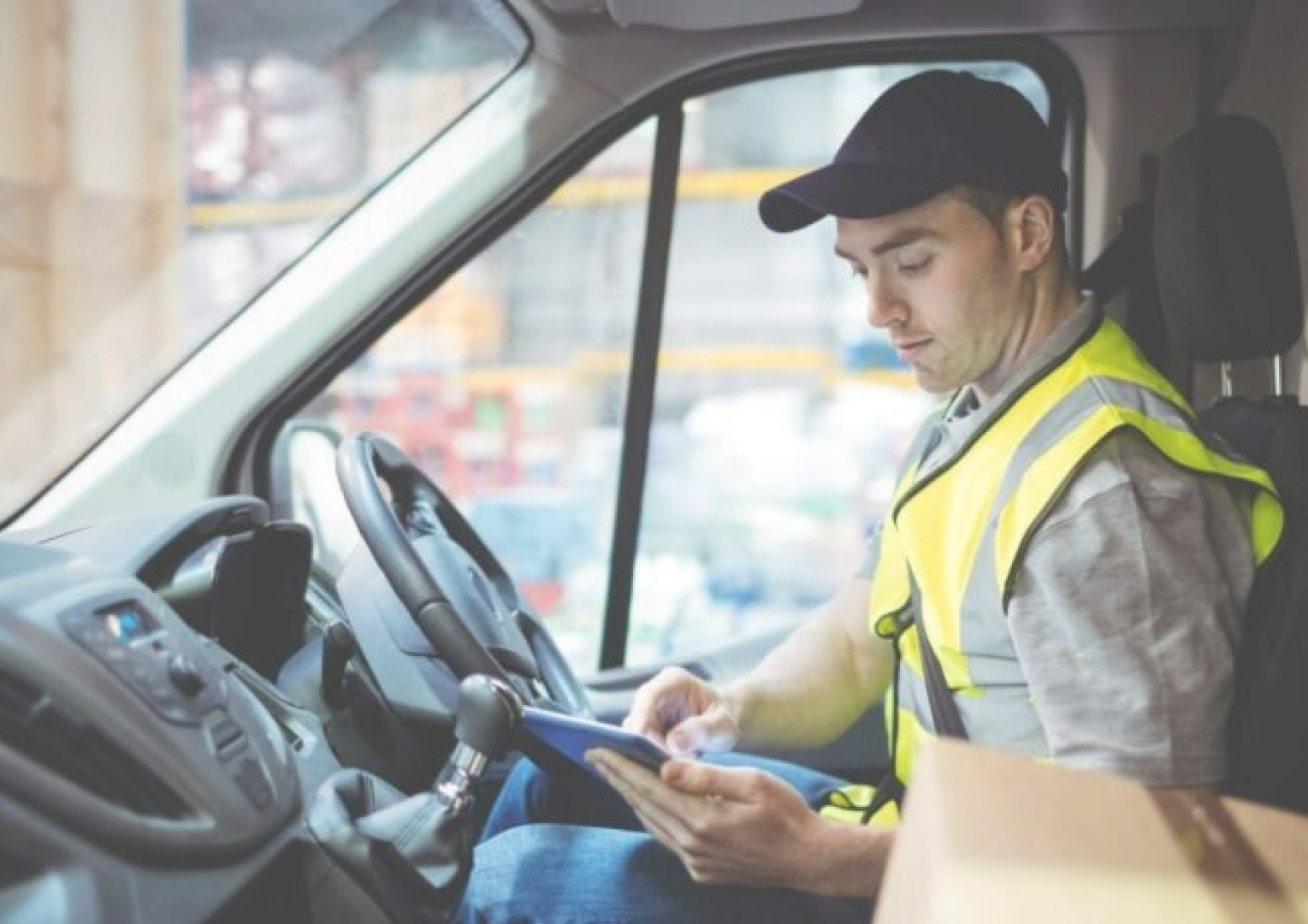 a courier driver looking at his phone. he is wearing a cap and a bright yellow safety jacket