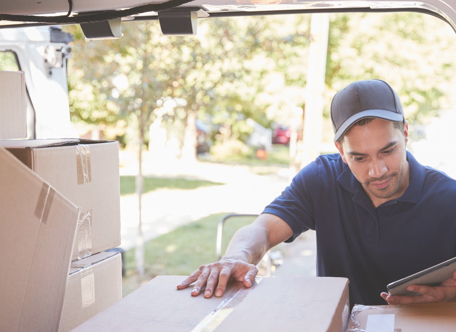 a courier driver in a dark cap checks parcels in the back of his van