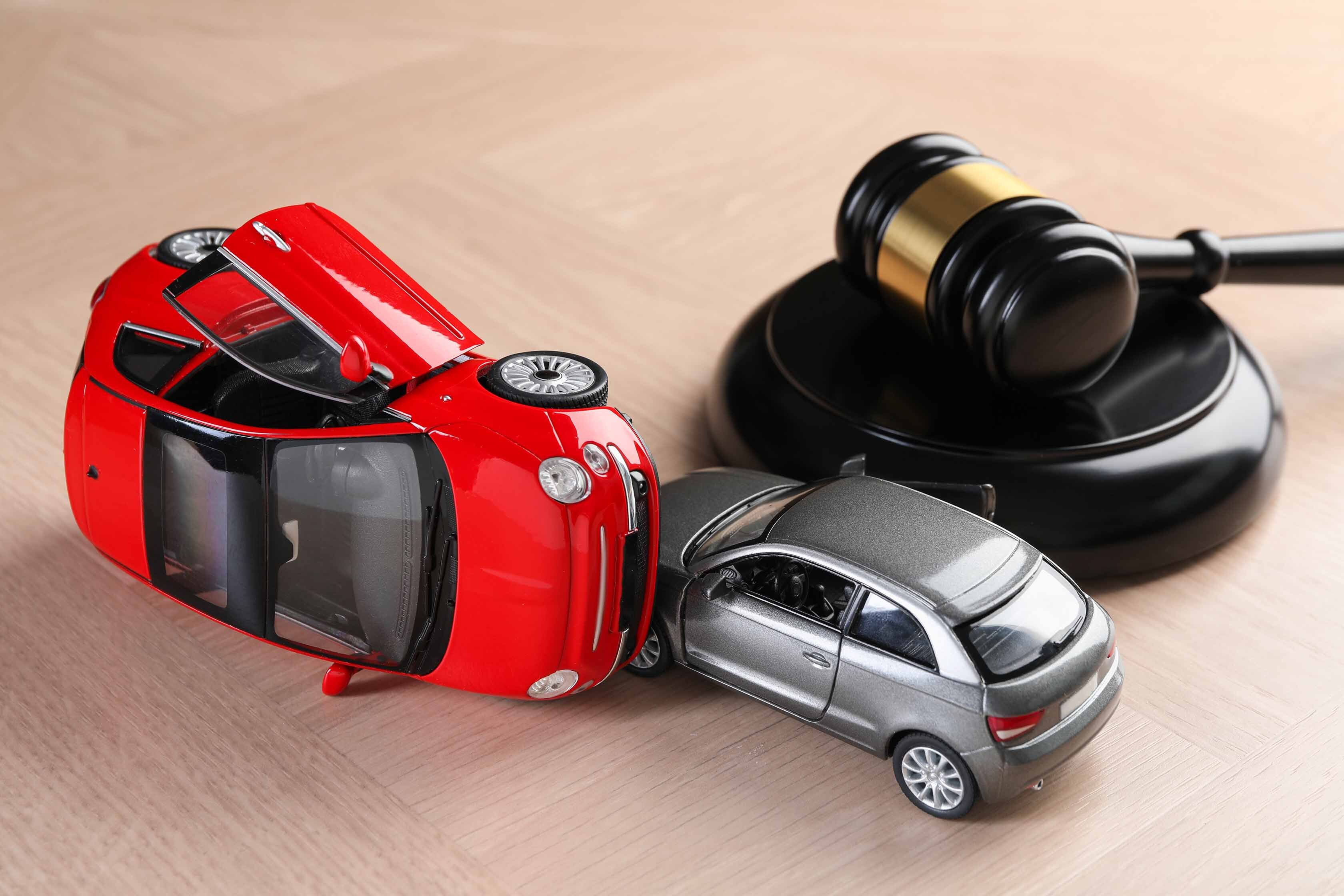 Two toys cars that have crashed into one another, with a gavel in the background