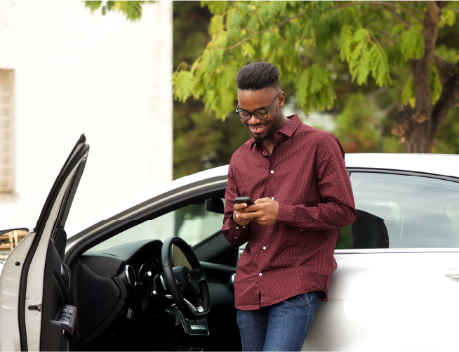 Driver leaning on vehicle looking at phone