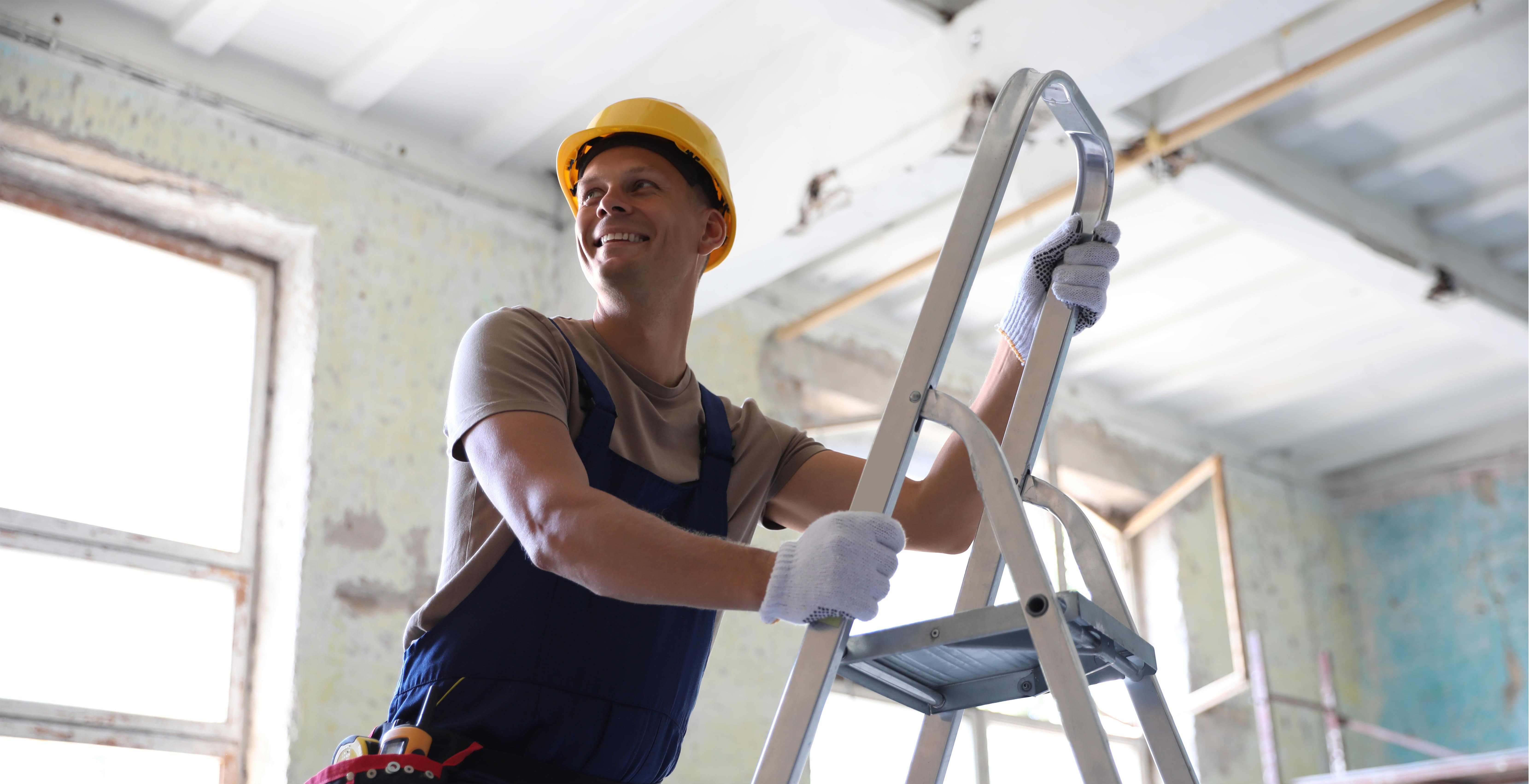 Smiling builder in hard hat standing on a ladder during interior renovation