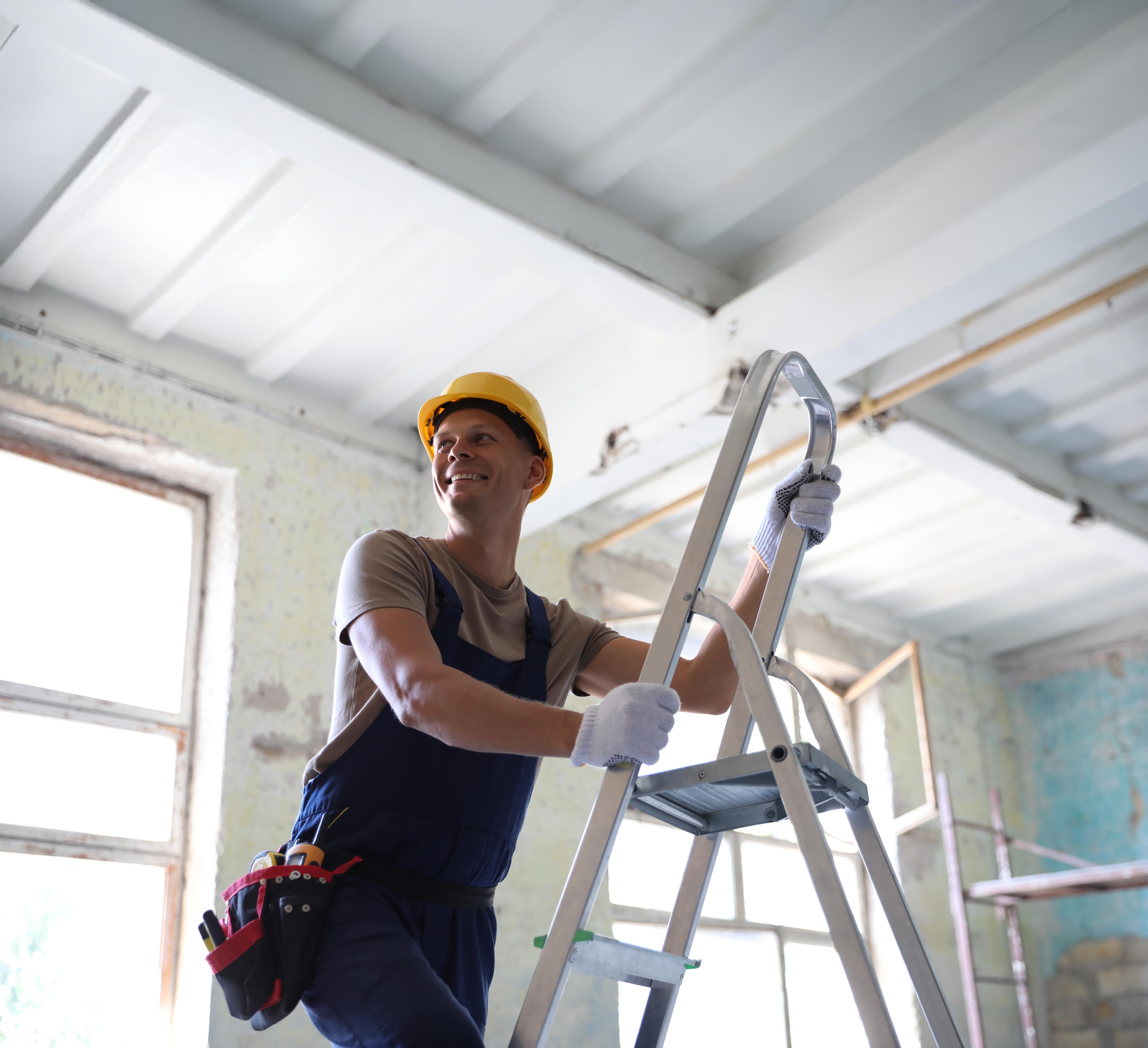 Smiling builder in hard hat standing on a ladder during interior renovation