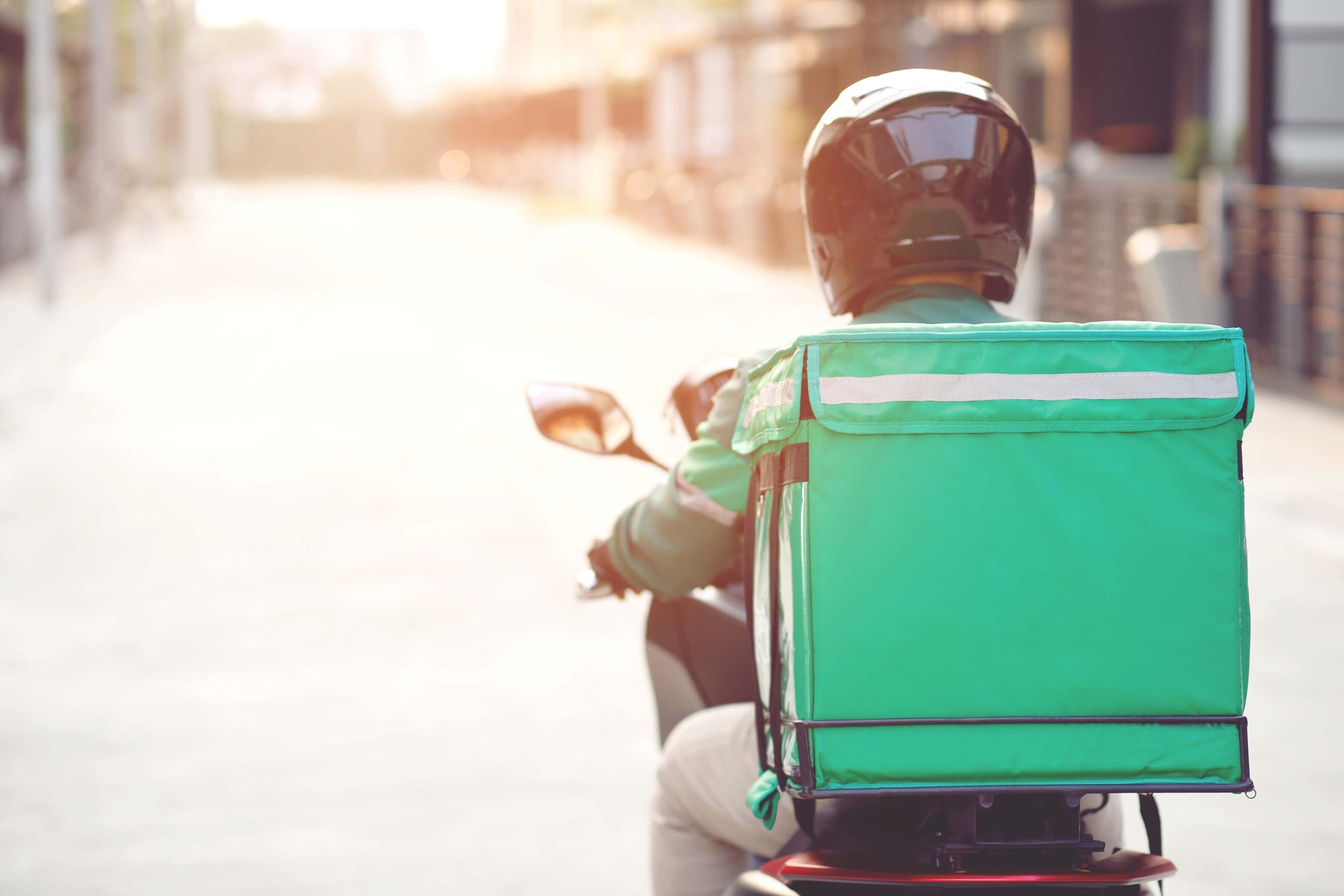 Back of a fast food delivery driver on a moped. they're wearing a fast food delivery bag on their back
