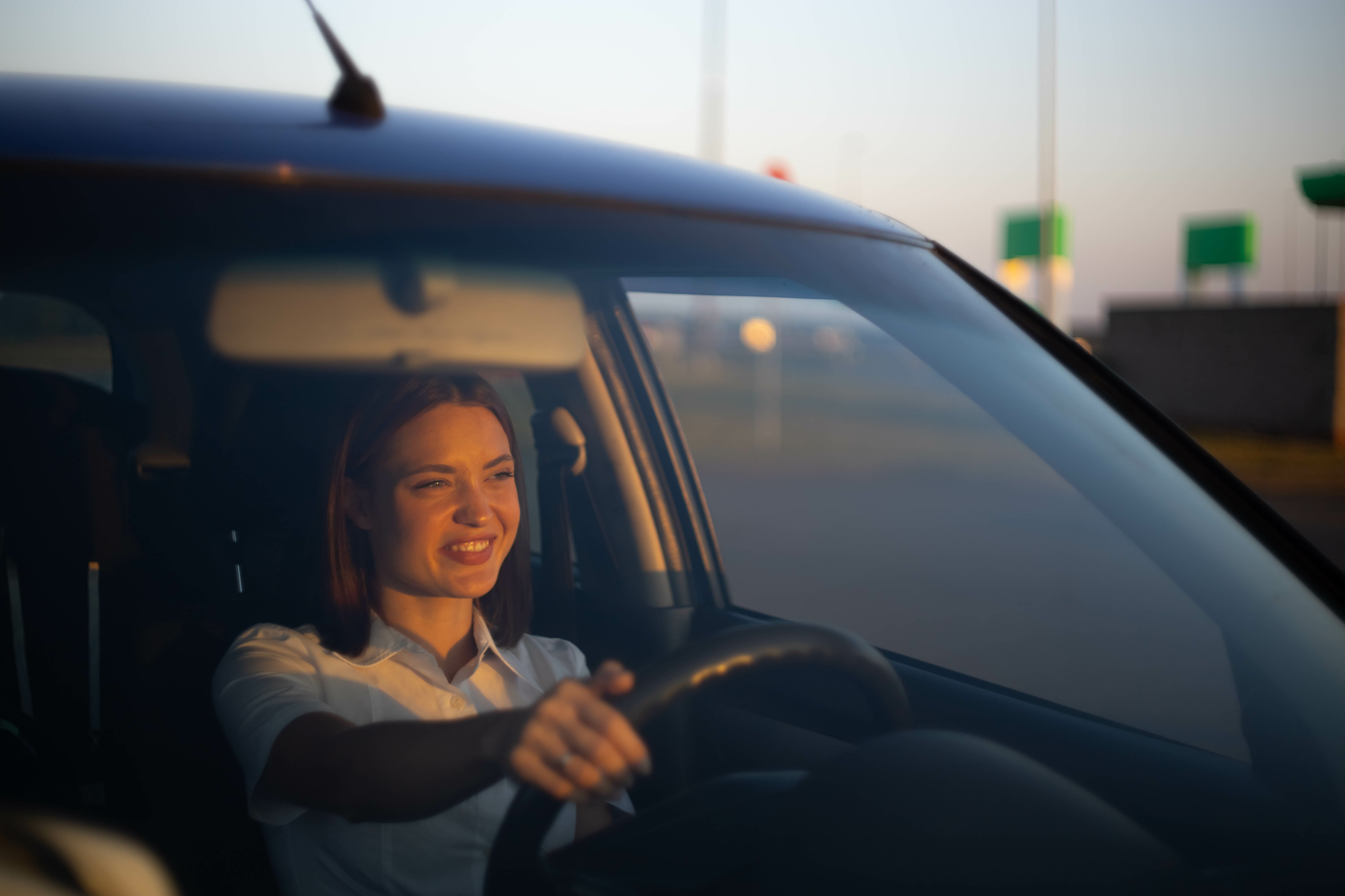 Smiling woman in the drivers seat of a car at sunset