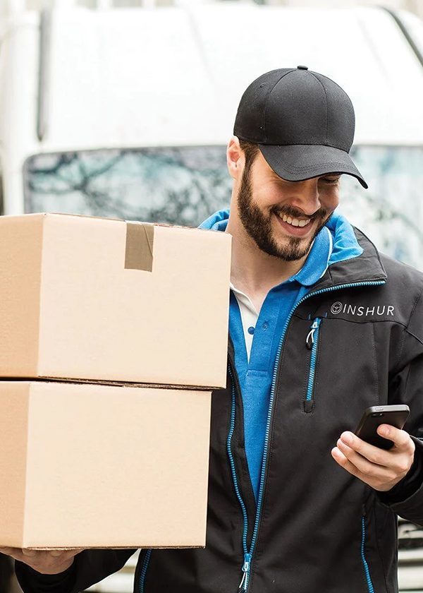 Courier driver in black jacket holdng parcels in one hand, checking his phone with the other
