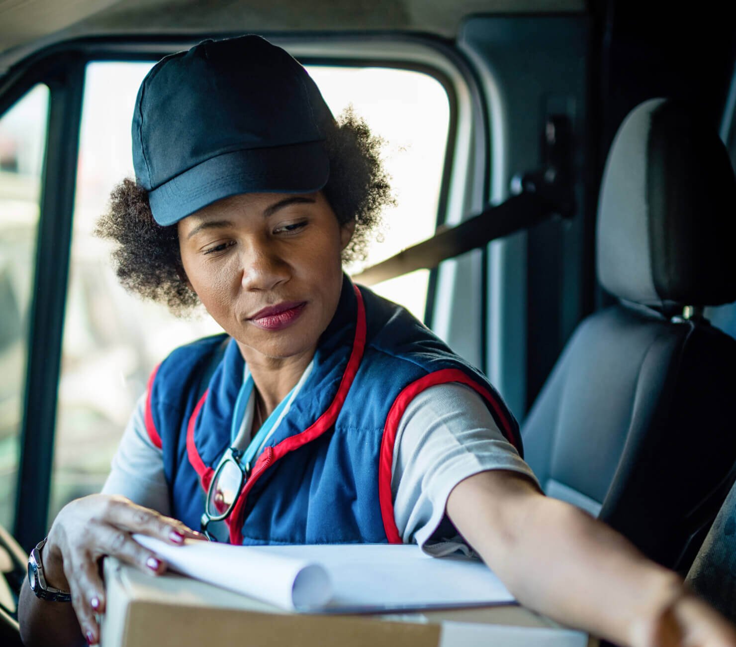 Delivery woman in blue uniform and cap with parcel in the driver's seat of a van