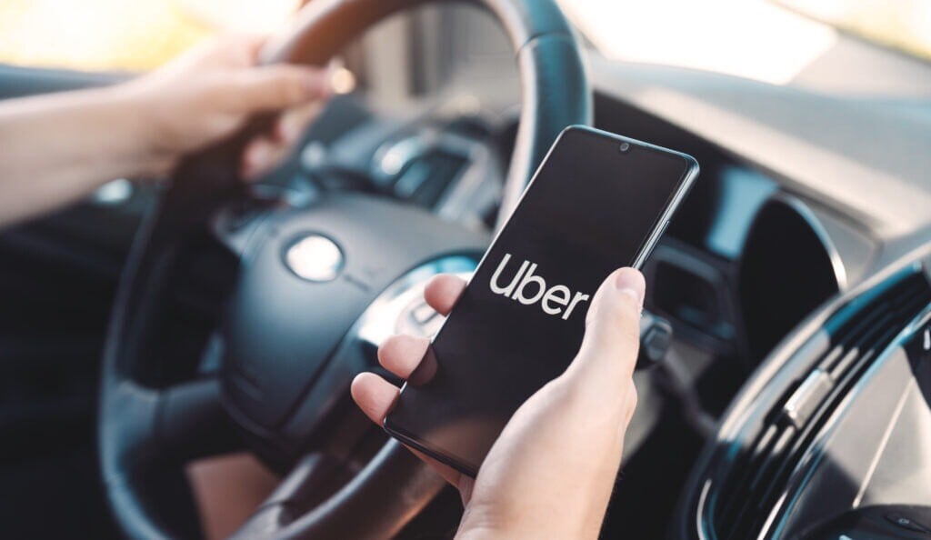 a hand holding a phone showing the uber homepage