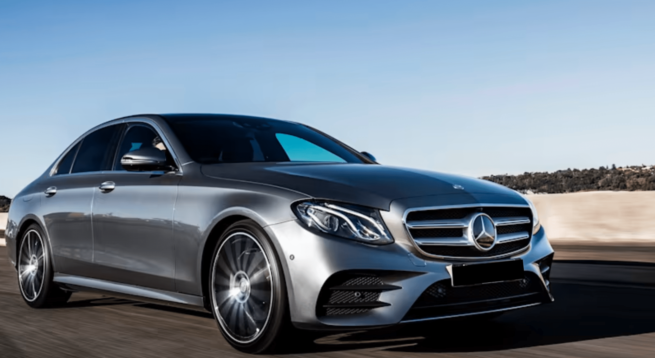 A silver Mercedes-Benz driving down the highway, beneath a clear blue sky