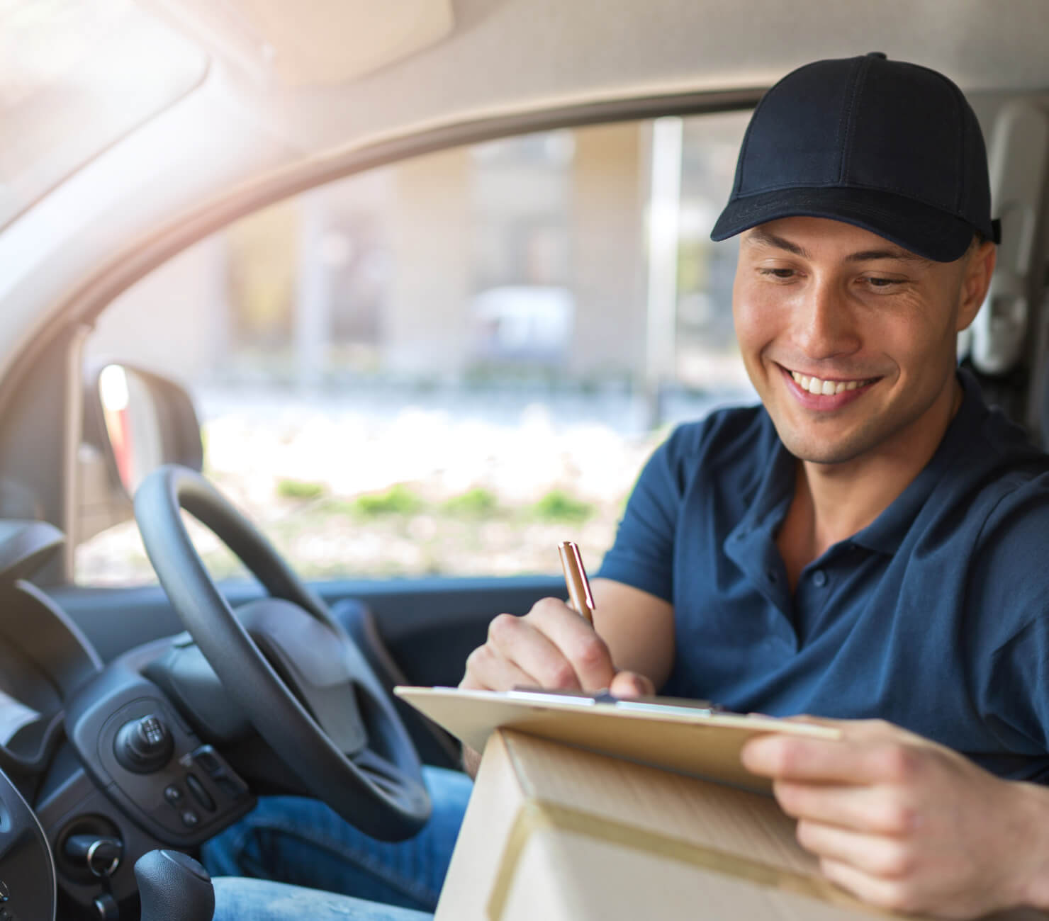 Man in blue shirt in the driver's seat of his car writing on a clipboard