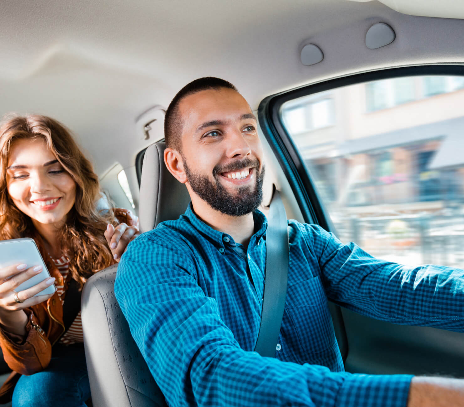 Driver in a blue, checked-shirt driving his smiling passenger to her destination