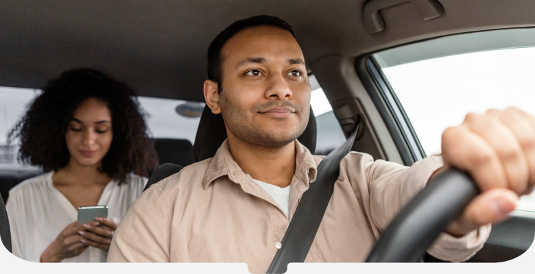 Smiling driver in a beige shirt and passenger who's looking at her phone