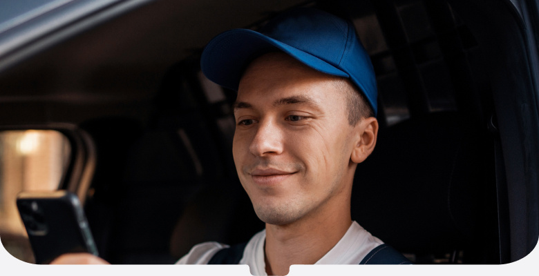 Driver in blue cap and overalls looking at his phone in his van