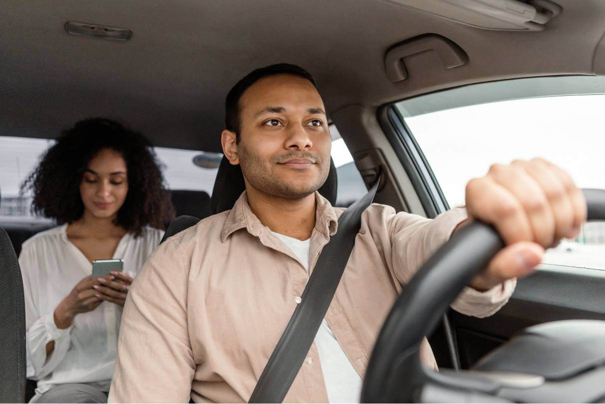 Man driving car with passenger on phone in back