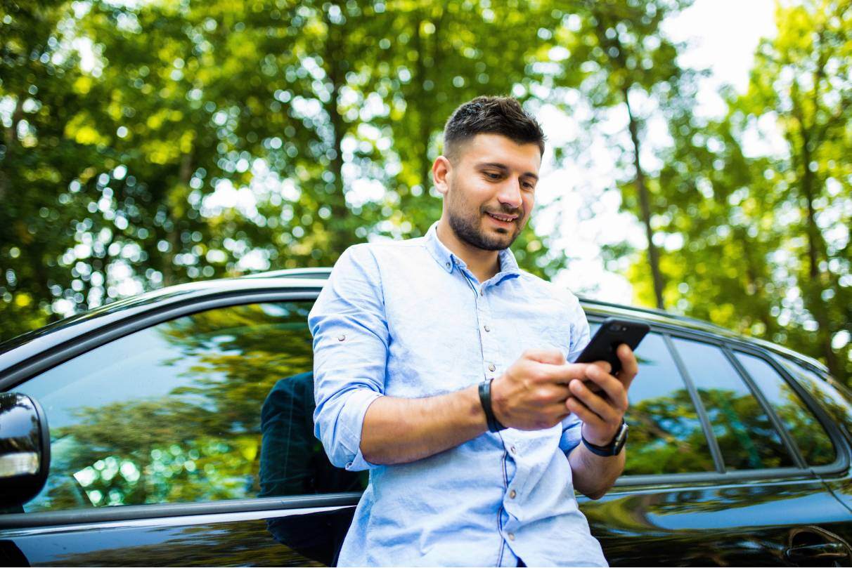 Man looking at phone leaning on car trees behind