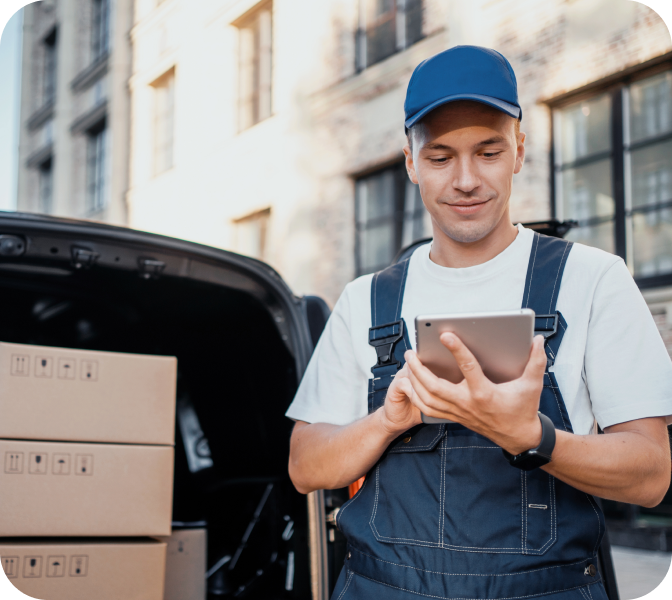 Man in overalls and blue cap standing next to his van and checking his tablet