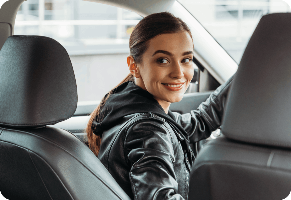 Woman in black leather jacket in the driver's seat of her car looking behind