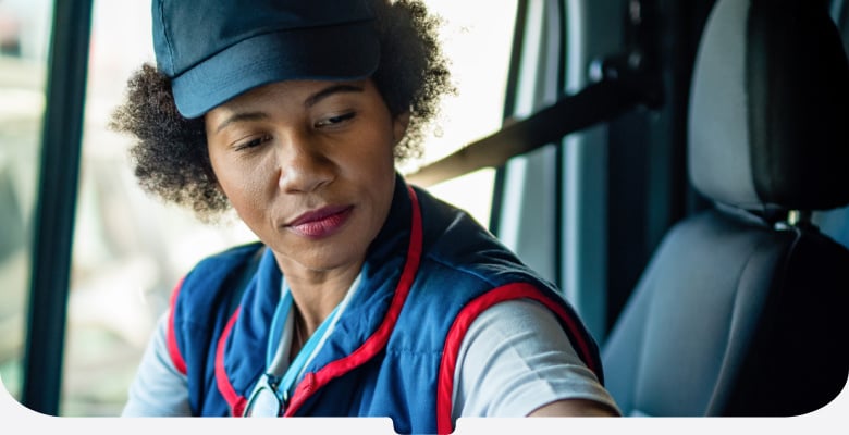 Delivery woman in blue uniform and cap with parcel in the driver's seat of a van