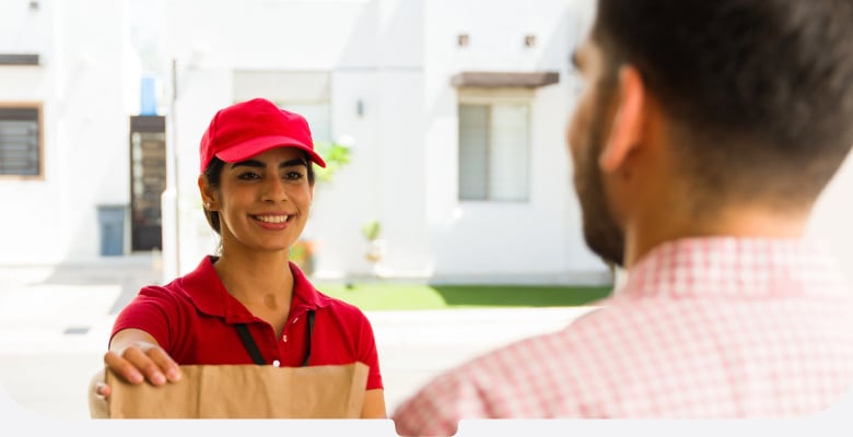 Food delivery woman in a red shirt and cap passing a paper bag to the recipient