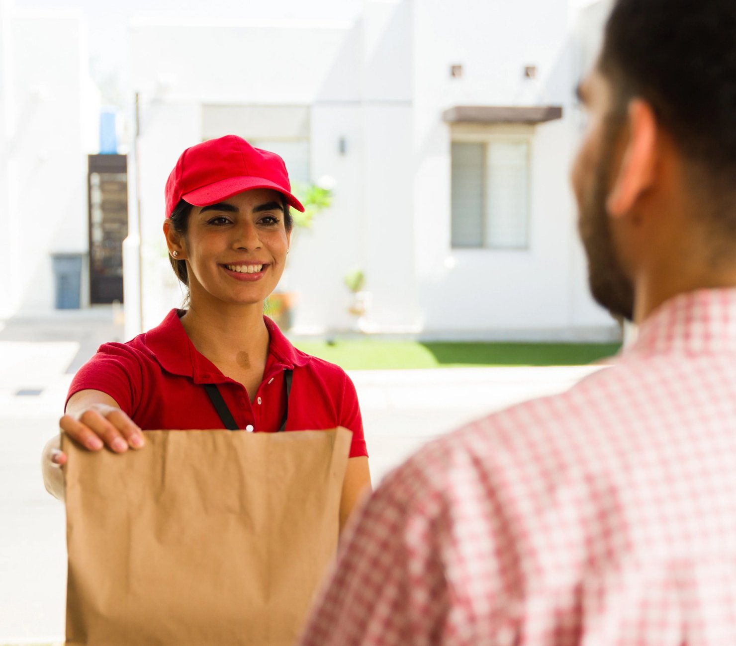 Food delivery woman in a red shirt and cap passing a paper bag to the recipient