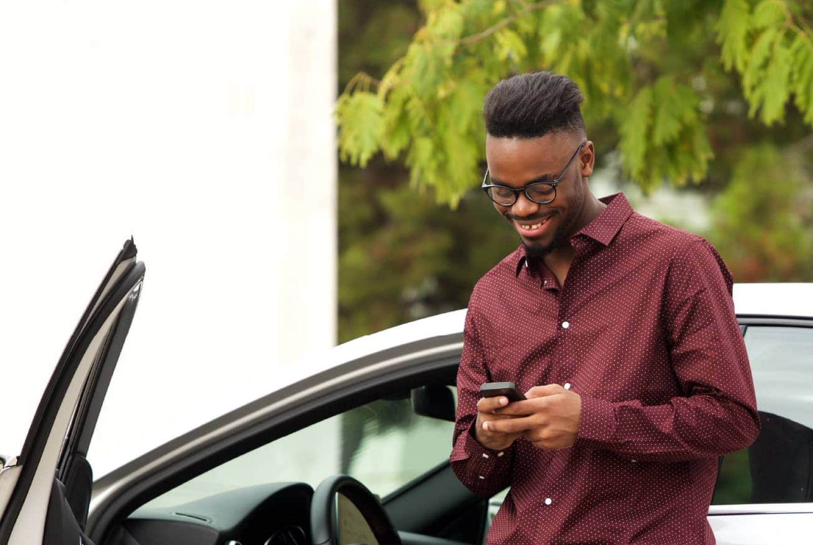 Man in red shirt leaning on car using phone