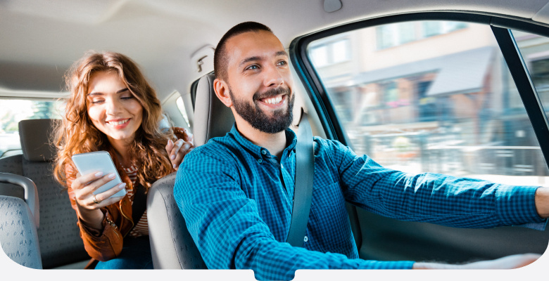 Driver in a blue, checked-shirt driving his smiling passenger to her destination