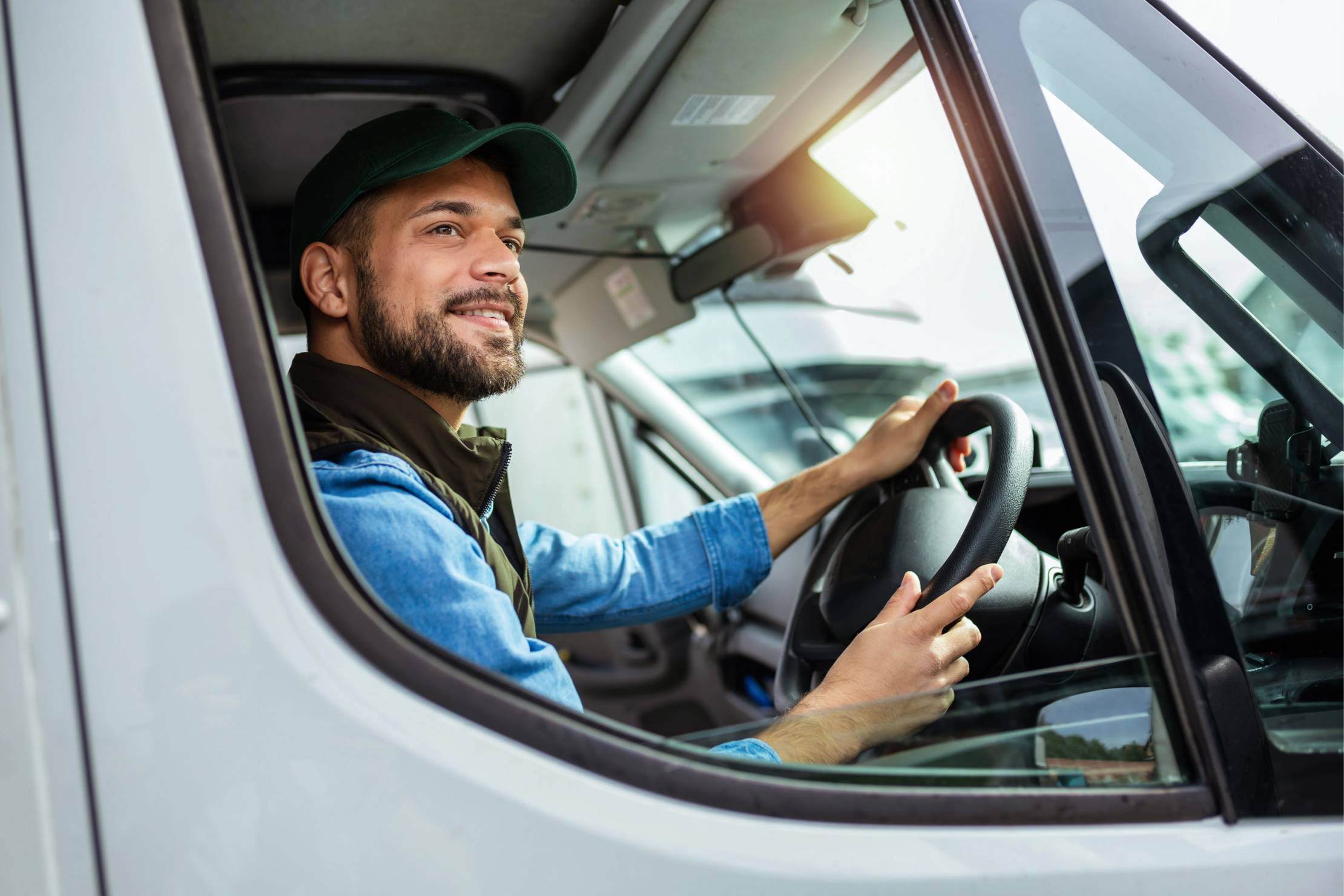 Bearded man in a blue denim shirt and black cap driving a van