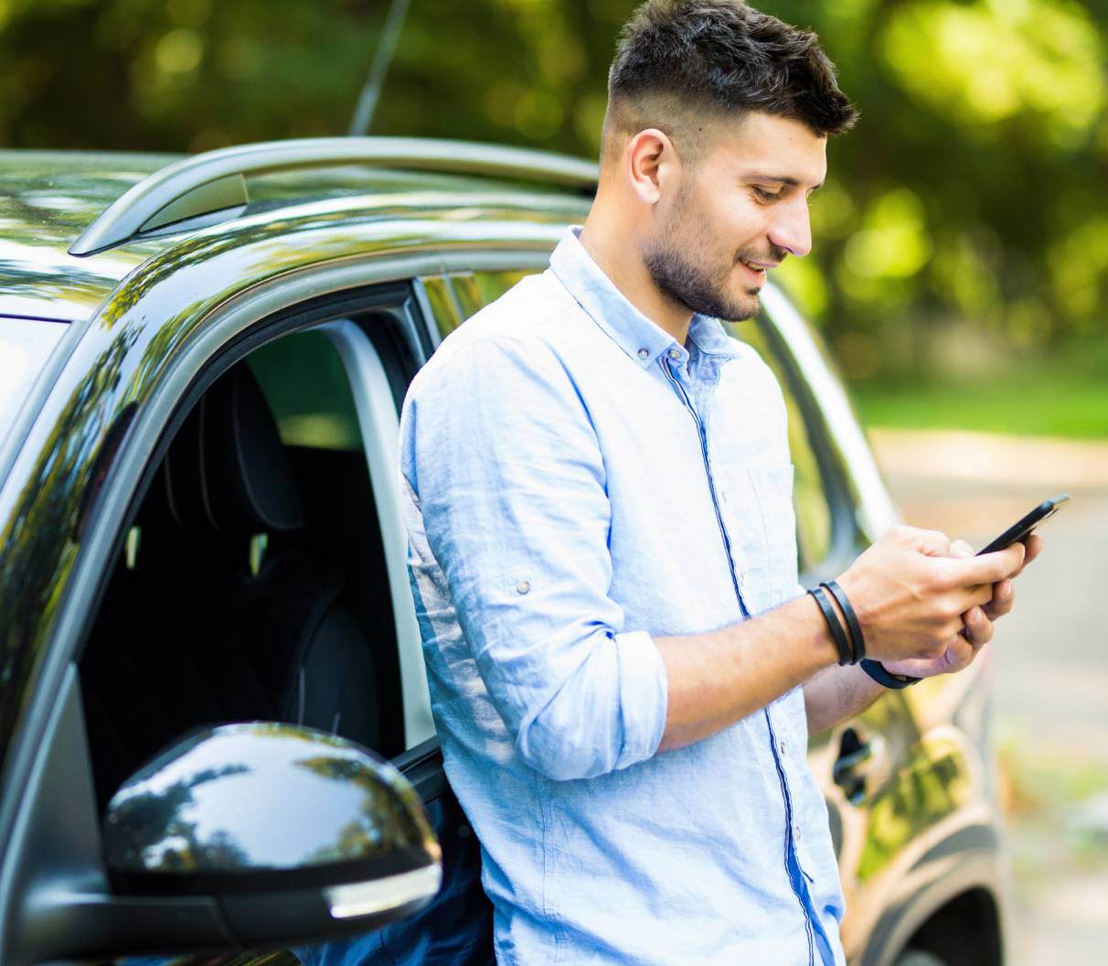 Taxi driver in a blue shirt standing next to his car while checking his phone