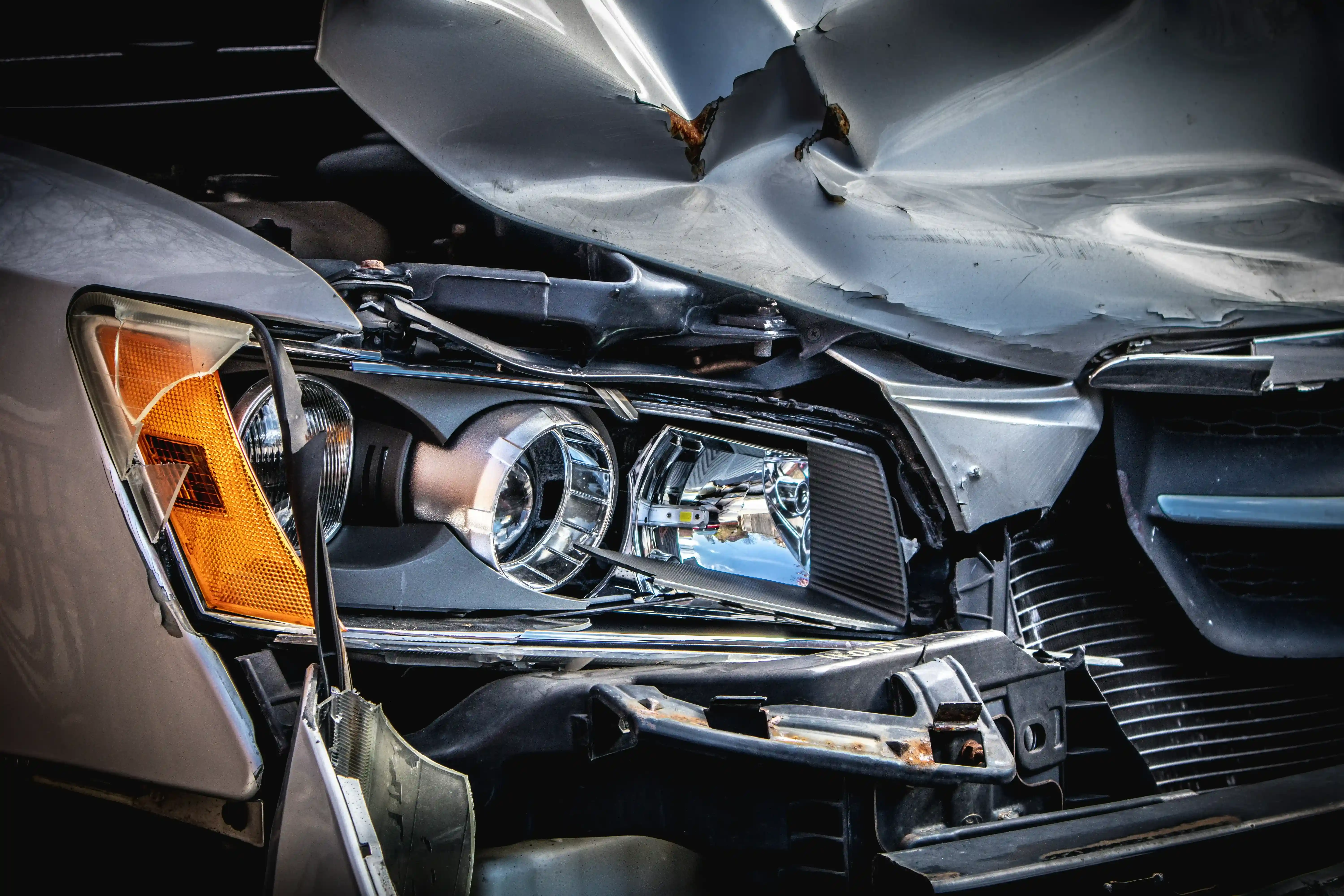 the scrunched bonnet of a silver car. Headlight is smashed and bonnet is severely damaged