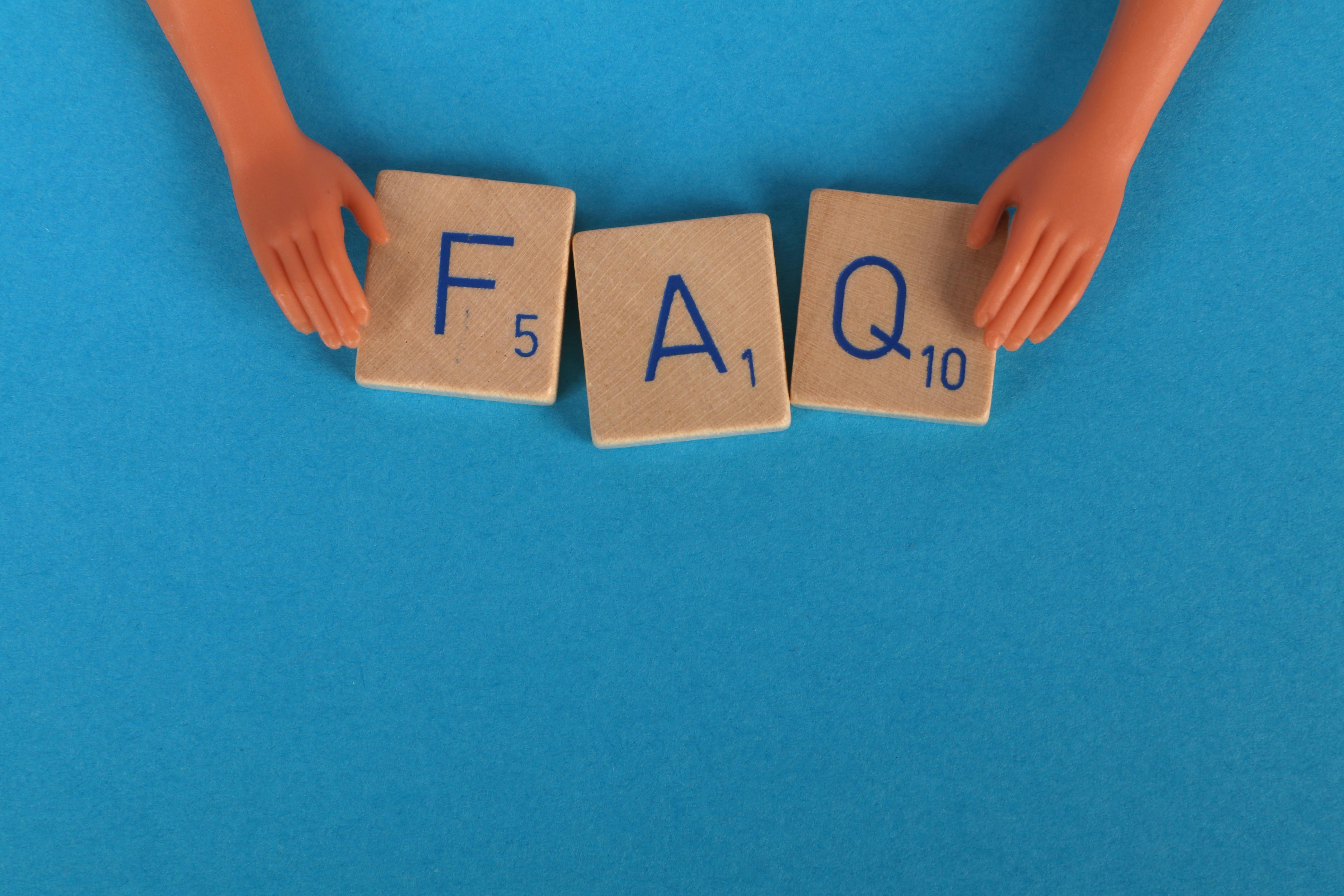 a pair of doll hands holding scrabble tiles that read F A Q on a blue background