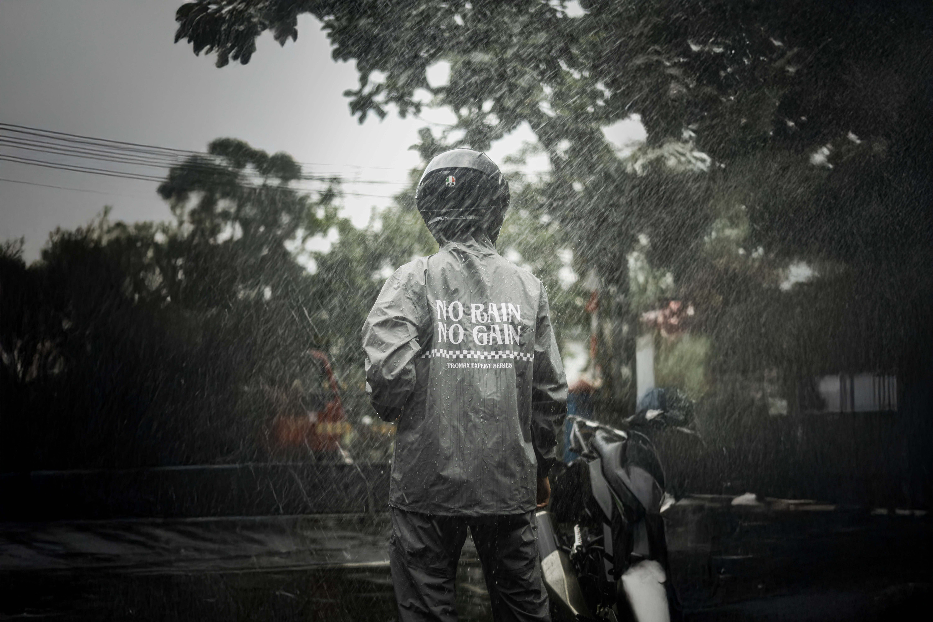 fast food delivery driver in the rain with a coat, facing away from camera that says No Rain, No Gain
