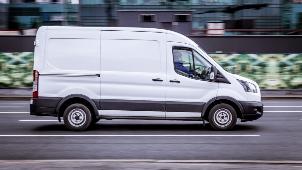 a side view of a white ford transit van driving on a city street